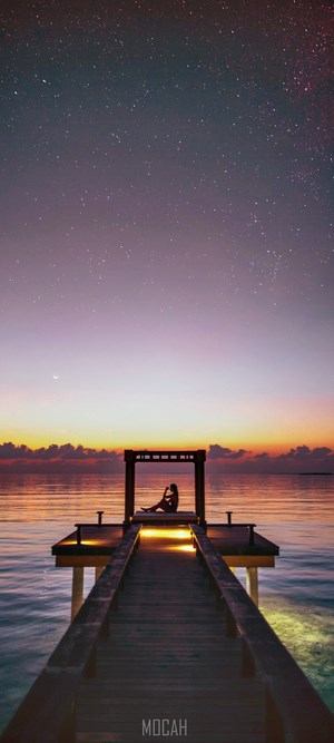 Woman on a pier under starry sky at sunset