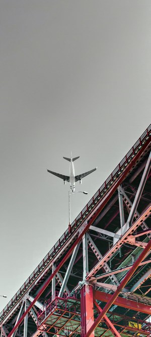 Airplane flying over a red steel bridge