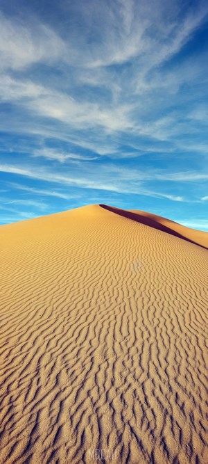 Sand dune under a blue sky with clouds
