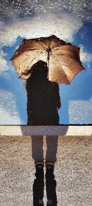 Reflection of a person with an umbrella in a puddle