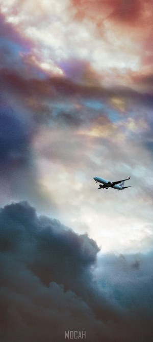 Airplane flying through colorful clouds at sunset