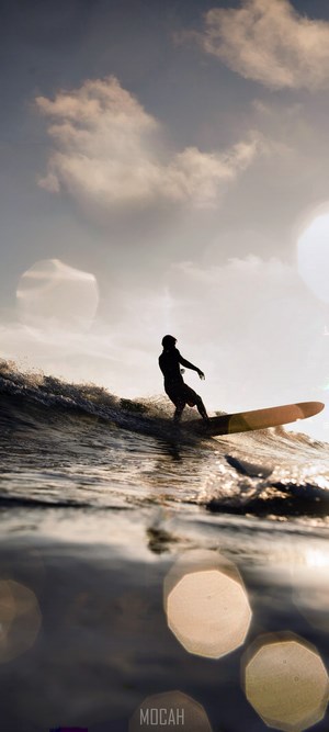 Silhouette of a surfer on a longboard riding a wave