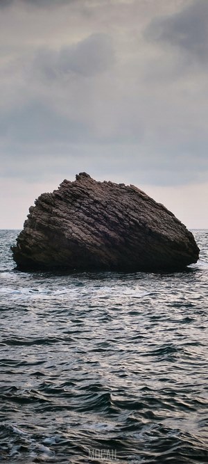Large rock in the sea under cloudy sky
