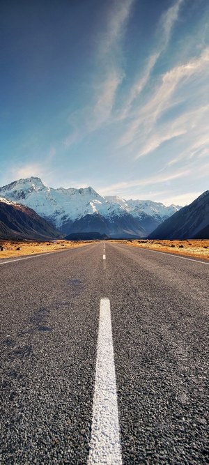 Road leading to snow-capped mountains under a blue sky
