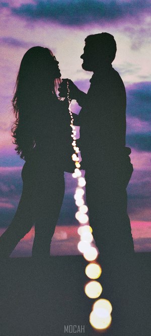 Couple silhouetted against a colorful sunset with bokeh lights