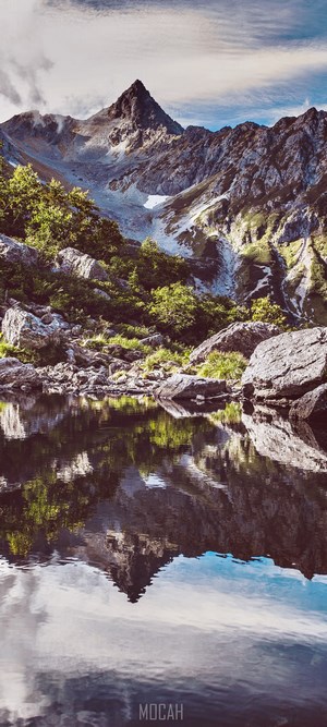 Mountain peak reflected in a calm lake with rocky shore