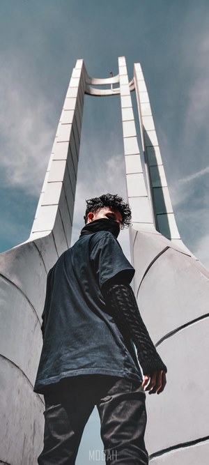 Man in mask and dark clothing in front of monument