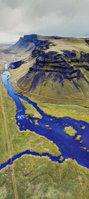 Sheep by a river near a cliff