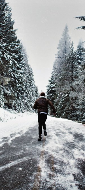 Man running on a snowy road between trees