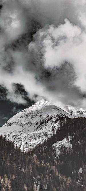 Snowy Mountain Peak with Dark Clouds and Forest