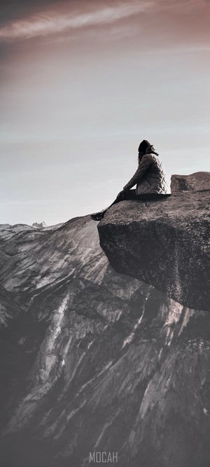 Person sitting on a cliff edge overlooking mountains