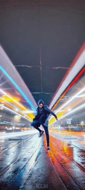 Person jumping on wet street with light trails