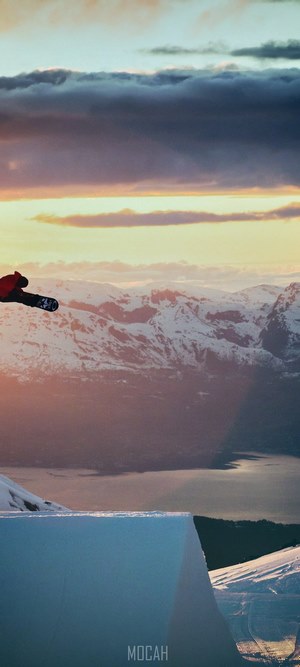 Snowboarder jumping over snowy mountains at sunset