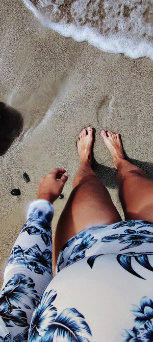 Person's legs and feet on a sandy beach with waves