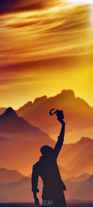 Silhouette of a person holding a camera against mountains and sunset