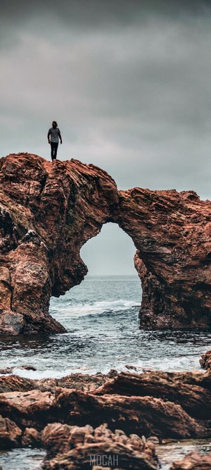 Person on rock arch over ocean