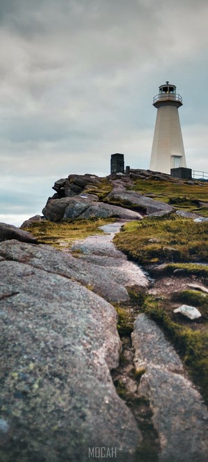 White lighthouse on a rocky coast under a cloudy sky