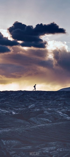 Hiker on lava field with dramatic clouds