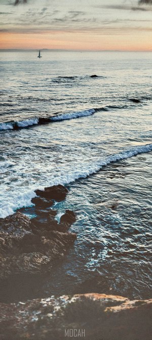Ocean waves crashing on rocks with sailboat at Crystal Cove
