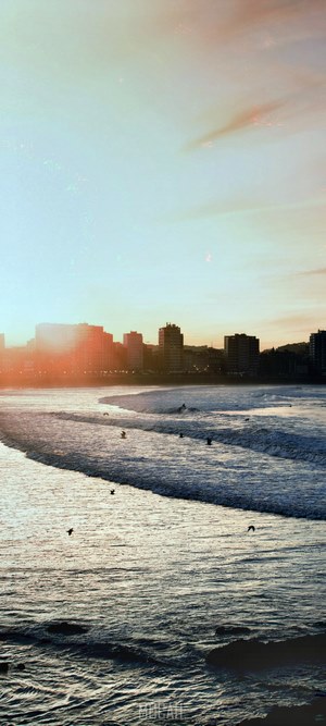 City skyline over ocean waves at sunset