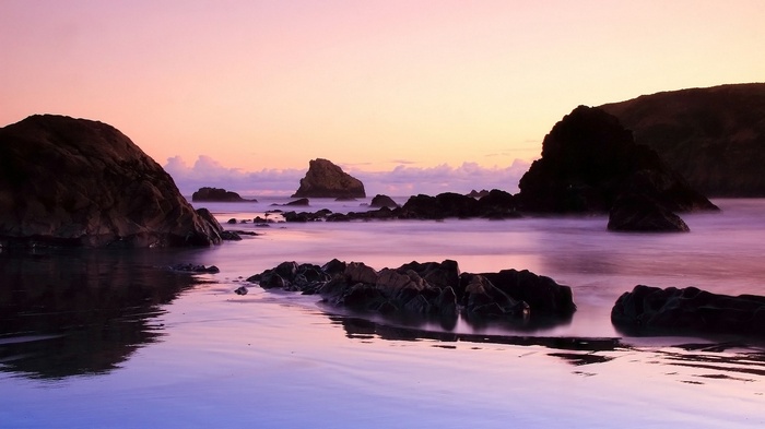 Ocean rocks at sunset with purple and pink sky