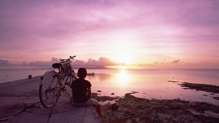 Person and bicycle watching sunset over the ocean