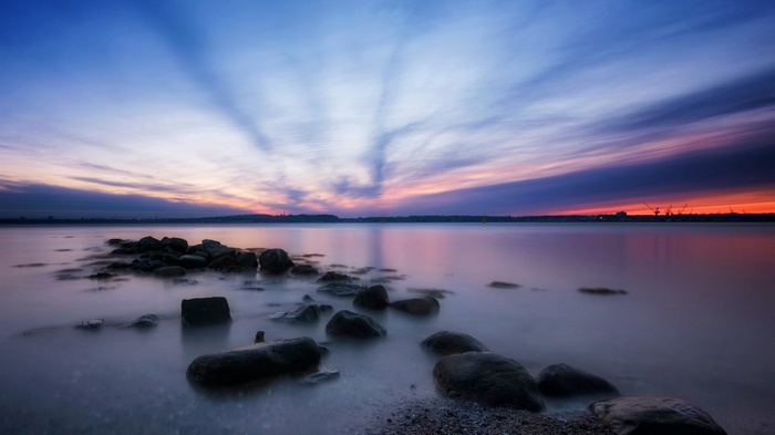 Sunset over a rocky shore with cranes in the distance