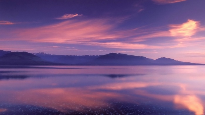 Purple and pink sunset over a calm lake and mountains