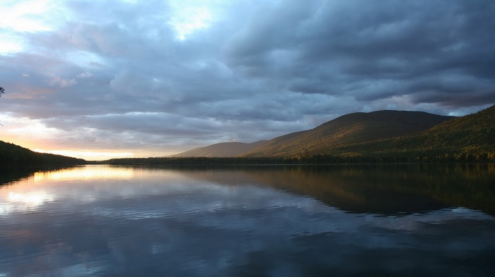 Lake and mountains at sunset with cloudy sky
