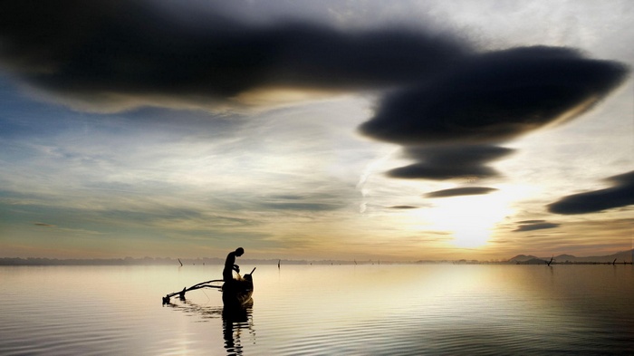 Fisherman in a boat at sunrise with dark clouds