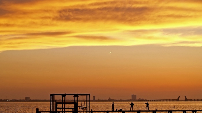 Fishermen on a pier at sunset with city skyline