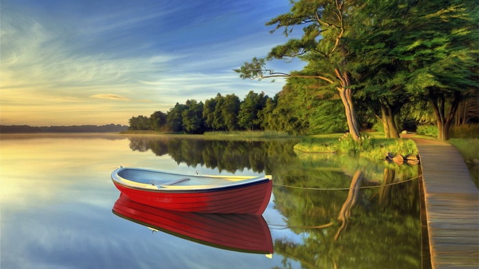 Red rowboat on a calm lake at sunrise with a wooden pier