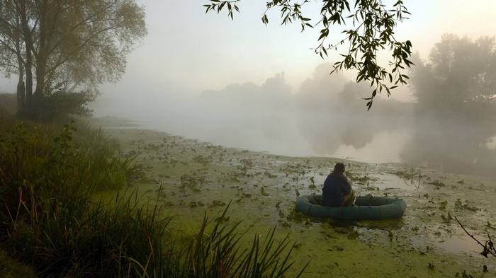 Man fishing in a foggy lake from a boat