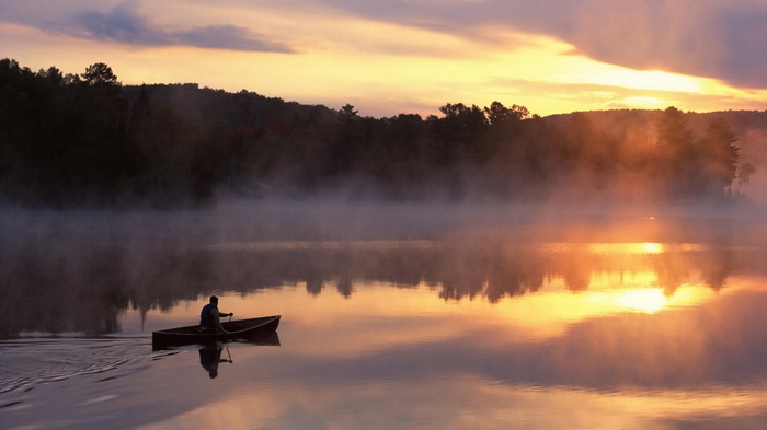 Man in canoe on misty lake at sunrise