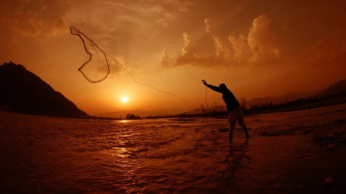 Fisherman casting net at sunset over river