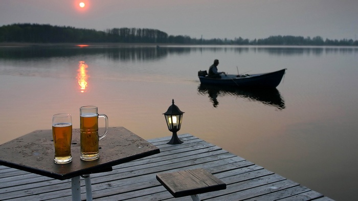 Two beers on a table by a lake at sunset