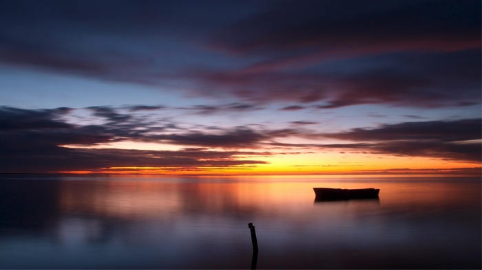 Boat on calm water at sunset with colorful clouds