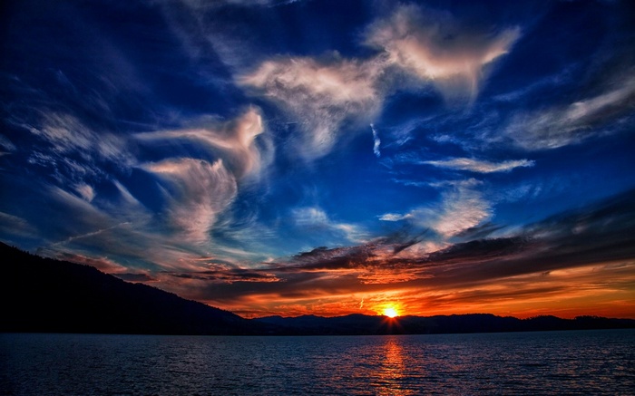 Sunset over a calm body of water with silhouetted mountains and dramatic clouds