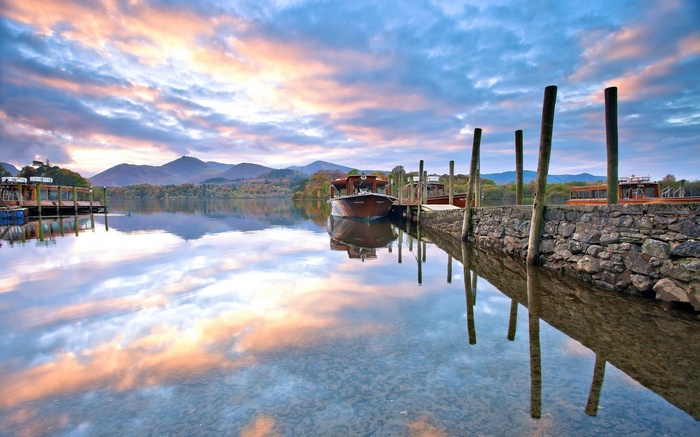 Boats docked on a lake at sunrise with mountain reflections