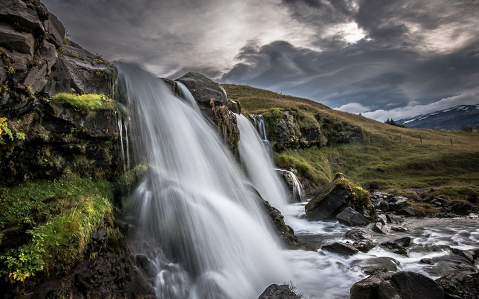 Waterfall cascading over rocks with stormy sky