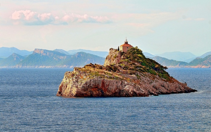Island with lighthouse and mountains in the background