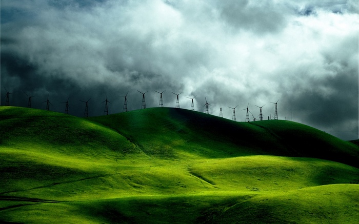 Wind turbines on green hills under stormy clouds