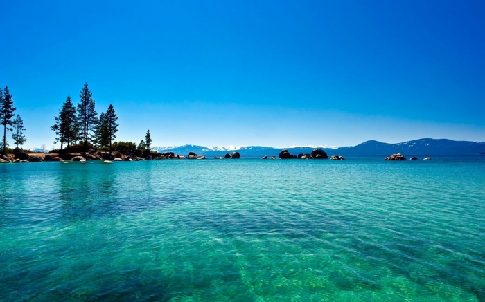 Turquoise lake with trees and mountains under a clear blue sky
