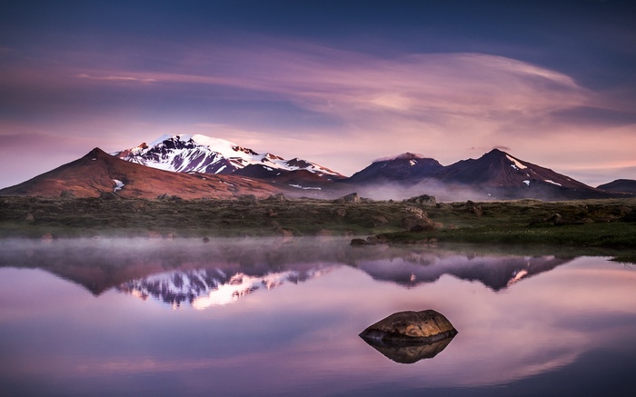 Misty mountains reflected in a calm lake at sunrise