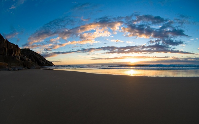 Beach at sunset with rocky cliffs and ocean waves