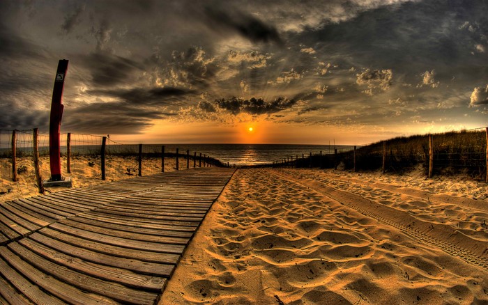 Wooden boardwalk and sandy path leading to the ocean at sunset