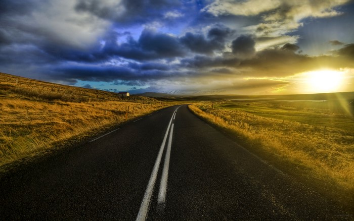 Road through a field at sunrise with clouds