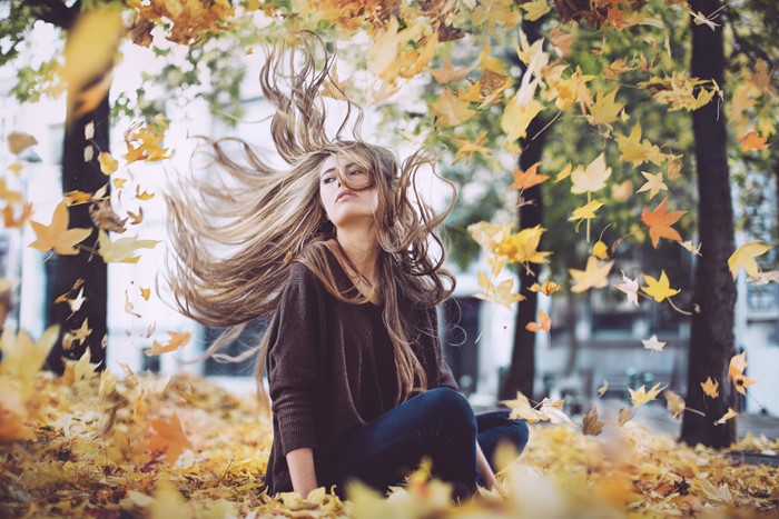 Woman sitting in fallen autumn leaves with windblown hair