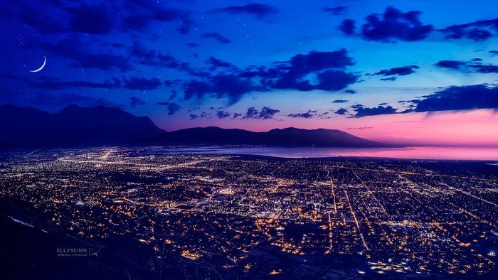 City lights at dusk with mountains and crescent moon