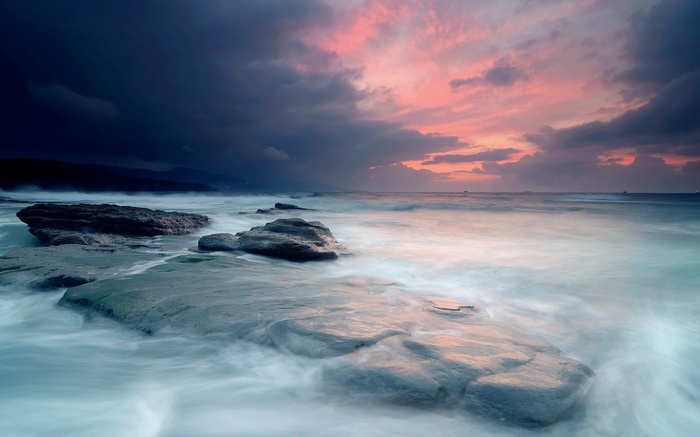 Ocean waves crashing on rocky shore at sunset